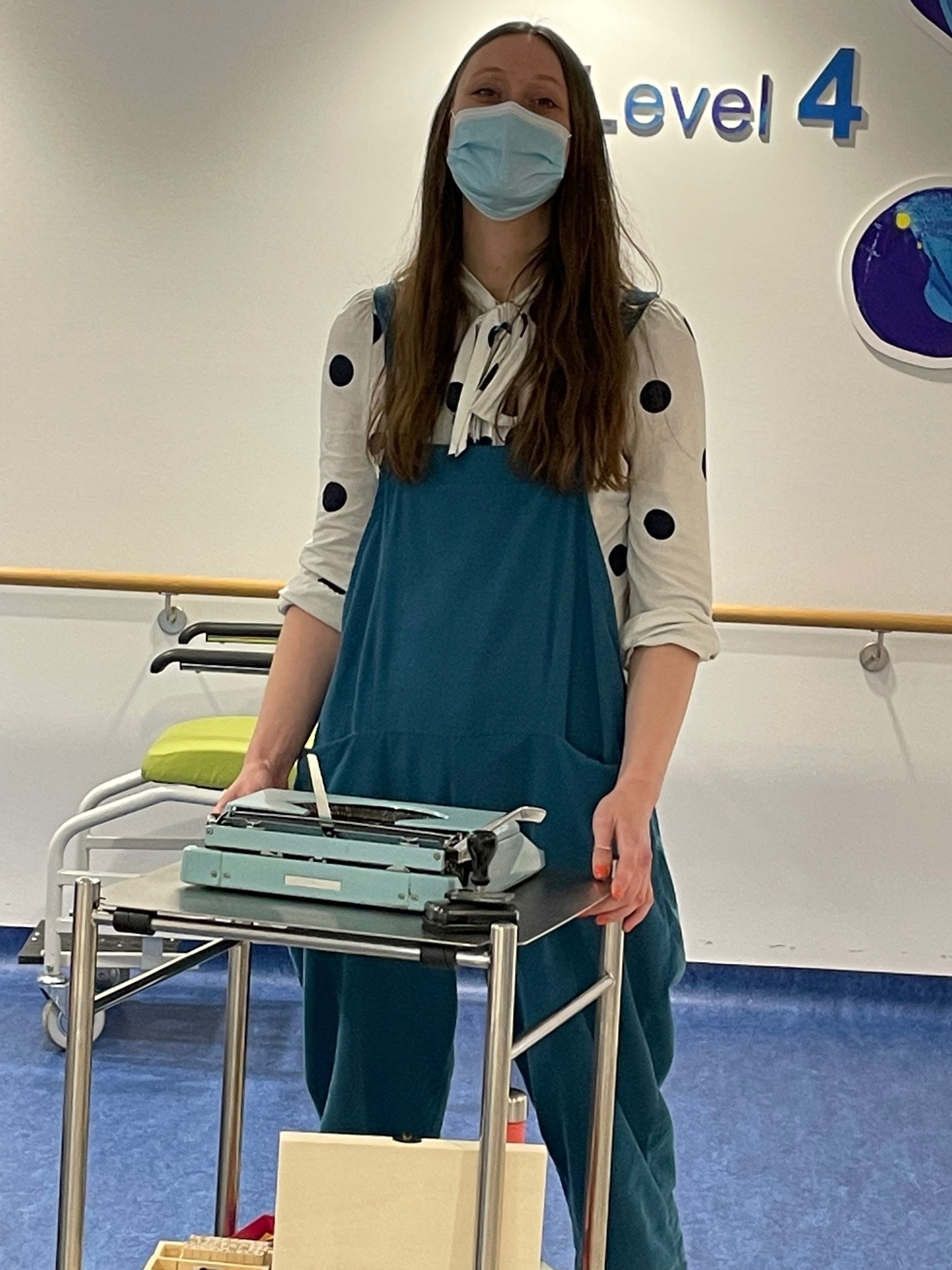 Woman pushing a trolley with a poetry machine on it in hospital corridor