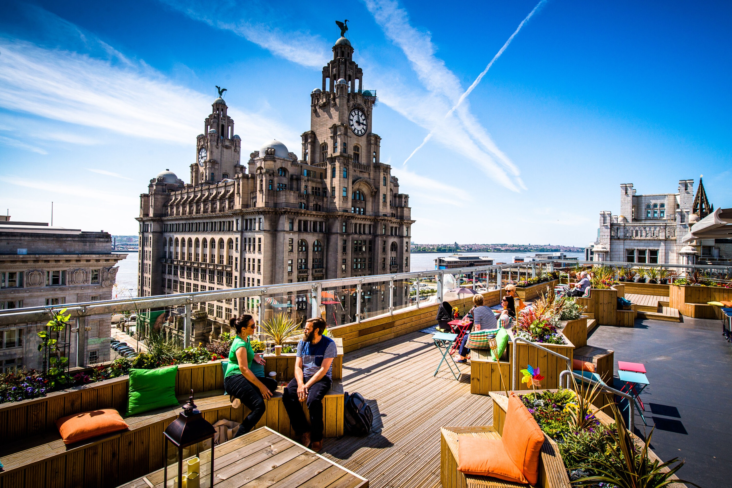 People relaxing in the Goodness Gracious rooftop garden with the famous Liver Building in the background