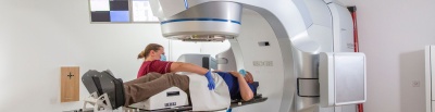 Therapeutic radiographer positioning male patient on treatment machine. The patient is lying on the treatment bed. The machine has a large arm that rotates around the bed to deliver the treatment.jpg