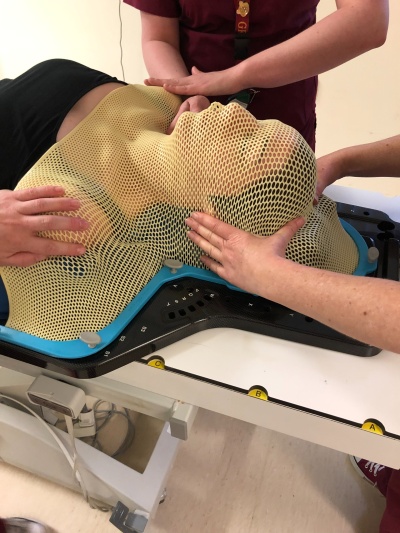 Patient with mask being fitted by two radiographers. The mask is made from a soft plastic and is perforated like a mesh with holes so people can breathe through it.