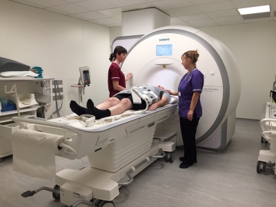 Person lying on MRI scanner table. There is a large ring-shaped machine behind him – this is the MRI scanner that will scan his body
